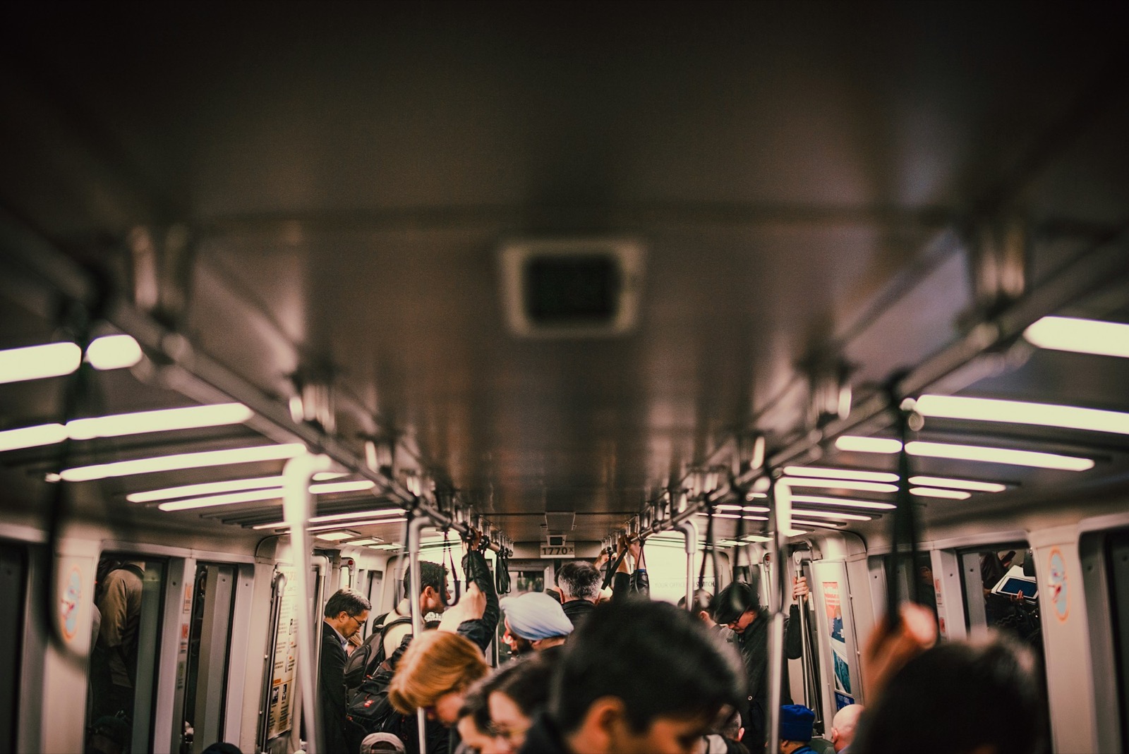 A busy commuter train carriage, passengers standing and holding the overhead rails.